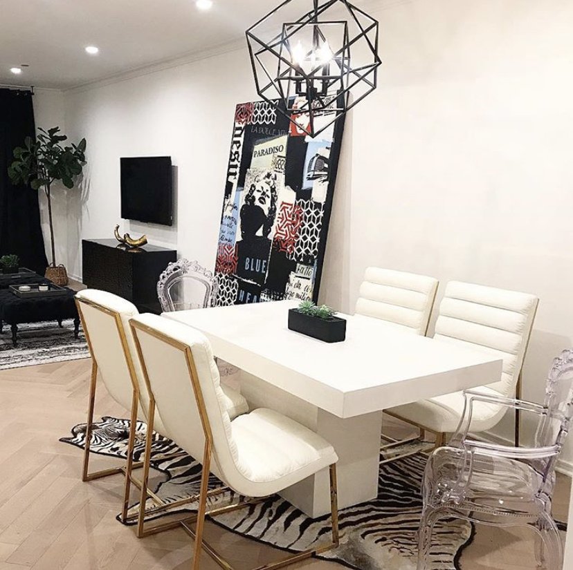 Dining room with white and gold chairs, a zebra-print rug, and an eclectic collage art piece