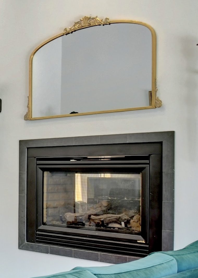 Detail of an arched gold mirror above a modern tiled fireplace