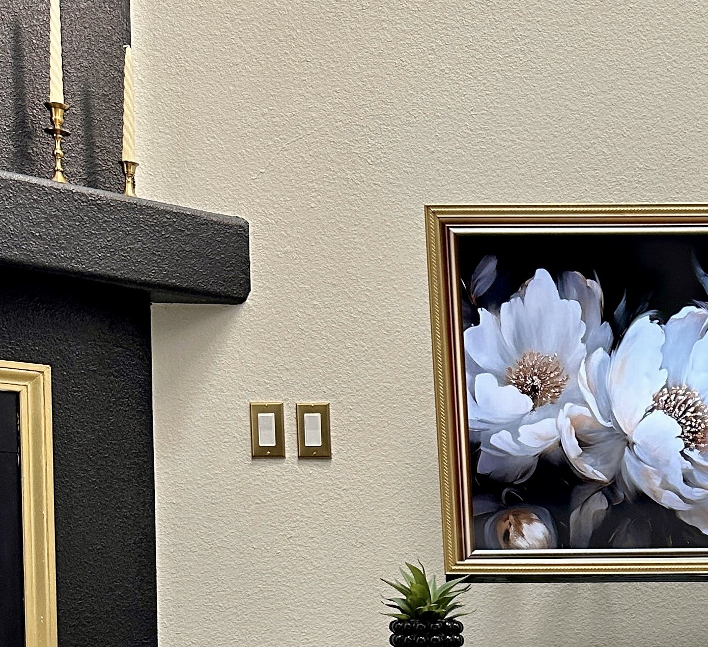 Detail of a framed floral painting and brass candlesticks on a black mantel