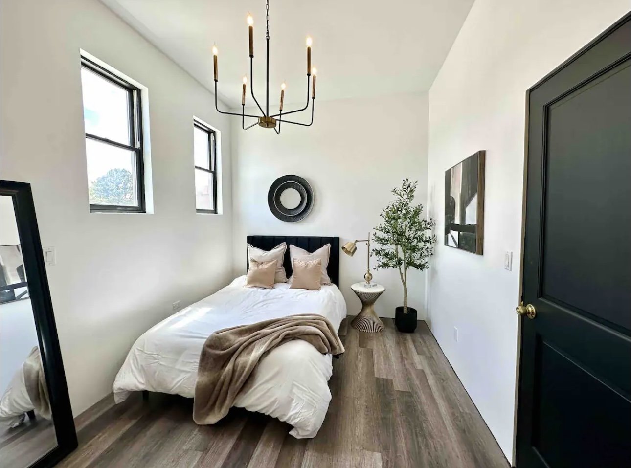 Bedroom with a black tufted headboard, round mirror, and olive tree