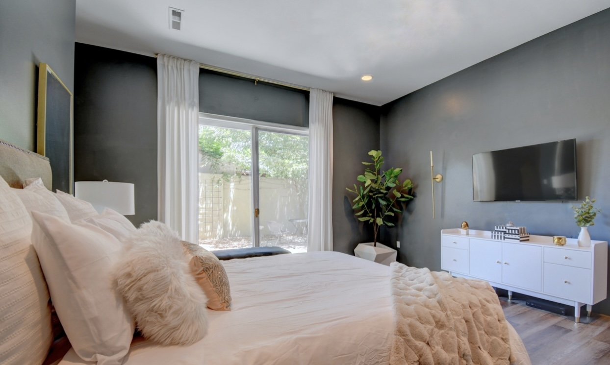 Bedroom with charcoal-painted walls, white linen curtains, and a sliding door to a private patio