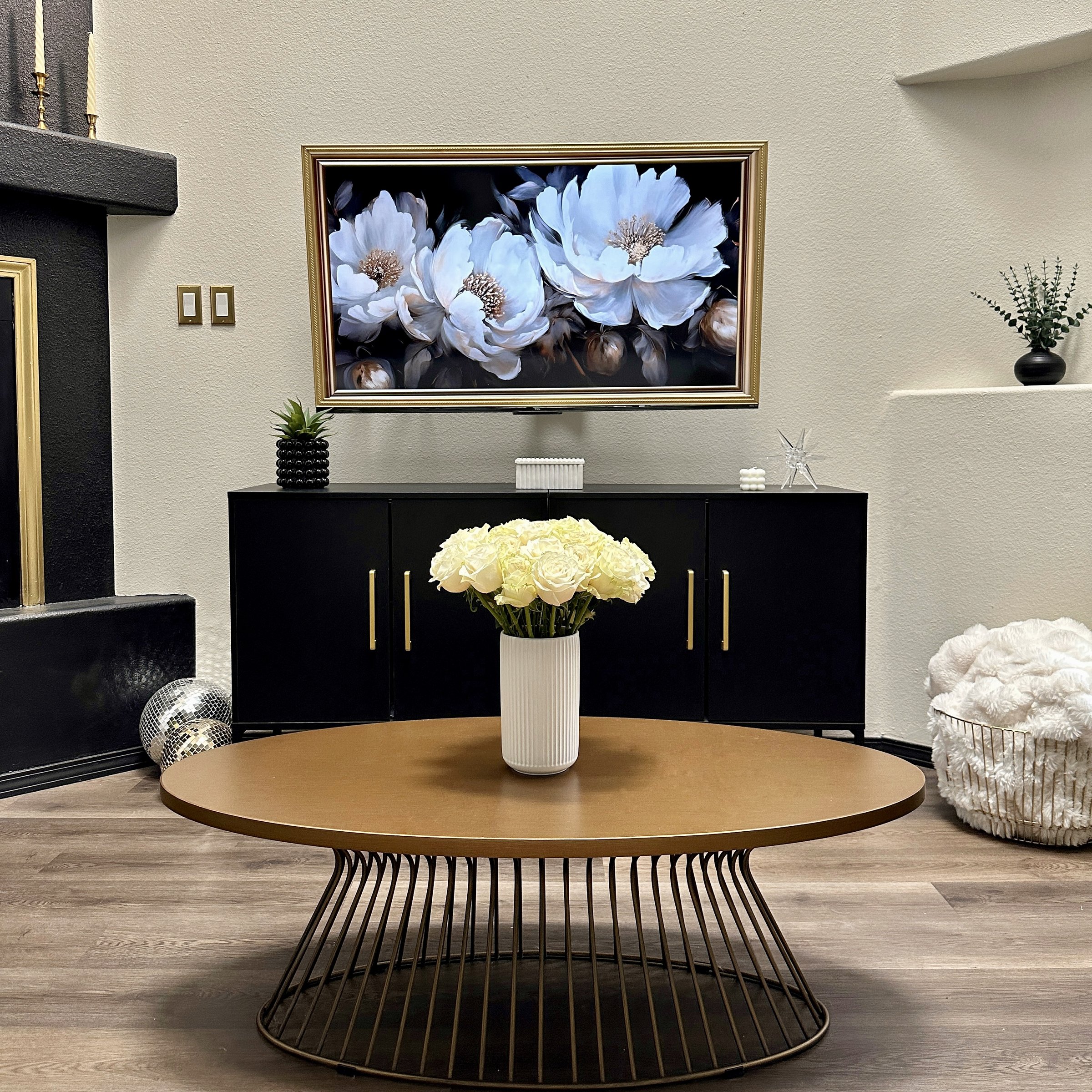 Moody black and gold living room vignette with a floral painting, black credenza, and round brass coffee table