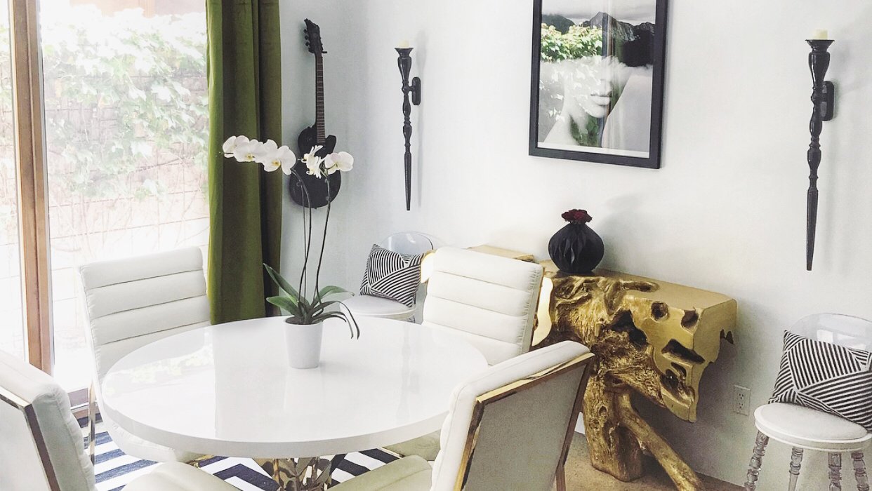Eclectic dining nook with a gold driftwood console, wall-mounted guitar, and orchid centerpiece