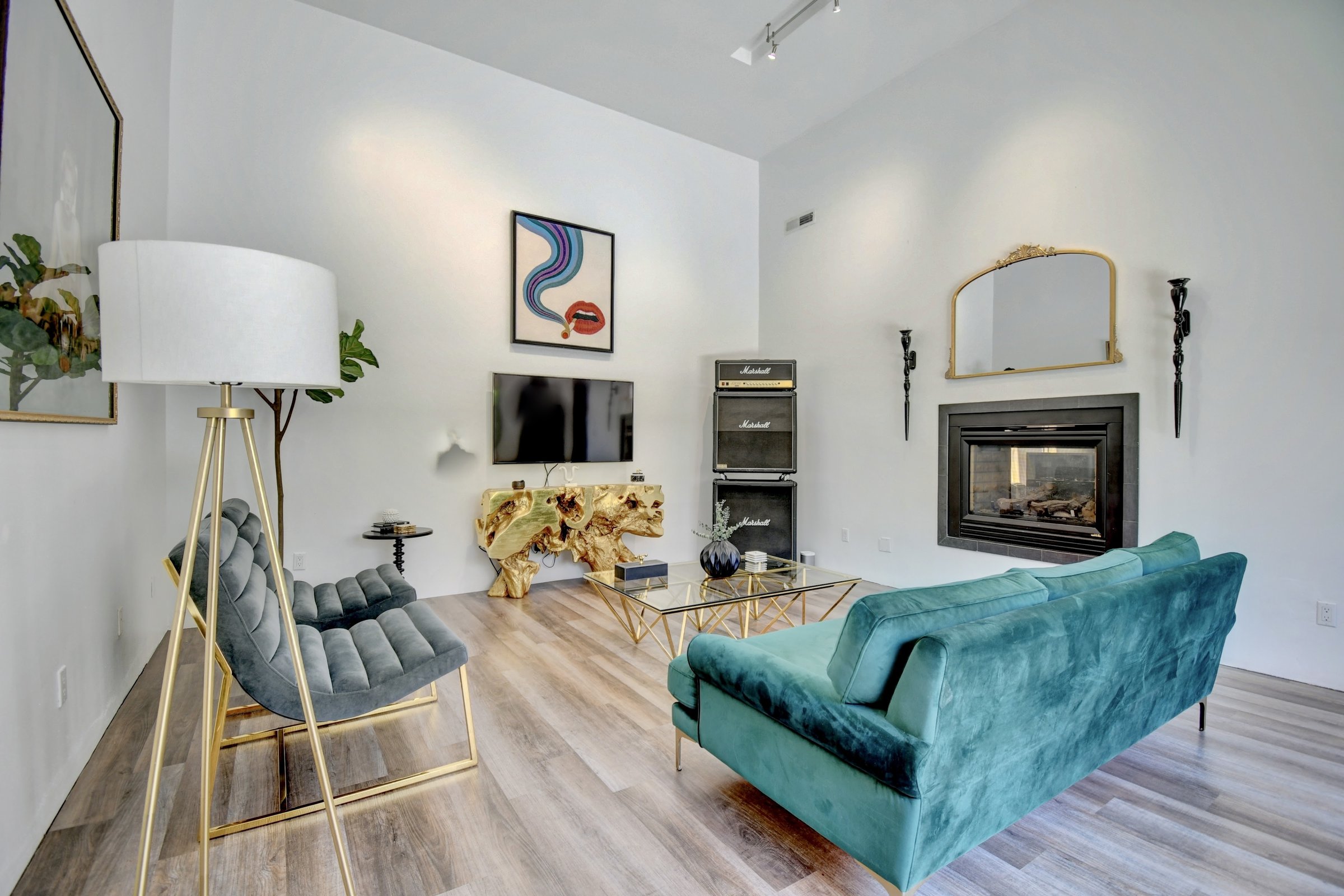 G Interiors hero photo — a glam living room with a teal velvet sofa, gold mirror, and fireplace